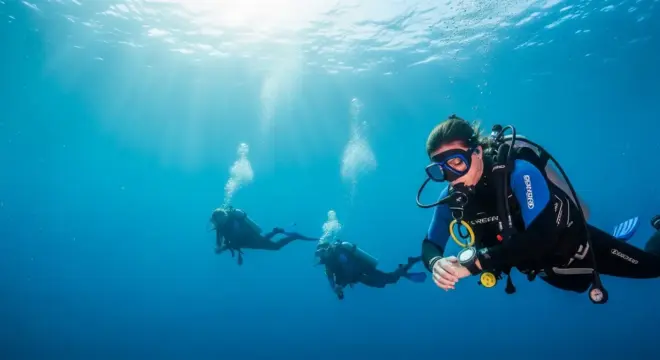 Buceadora consultando su ordenador de buceo mientras otros dos buzos nadan en el fondo del océano azul.